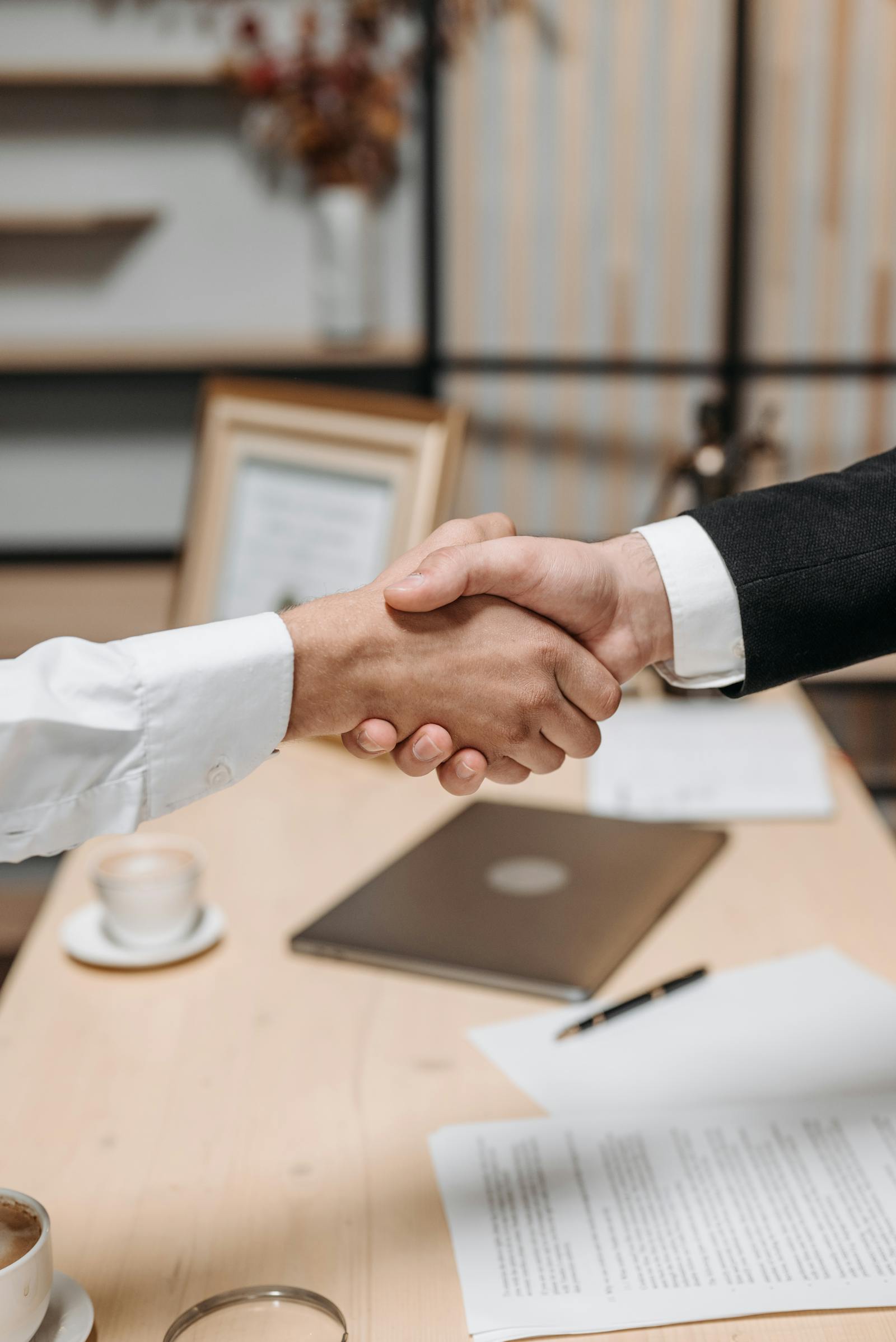 Handschlag zweier Geschäftspartner über einem Schreibtisch als Zeichen der Zusammenarbeit